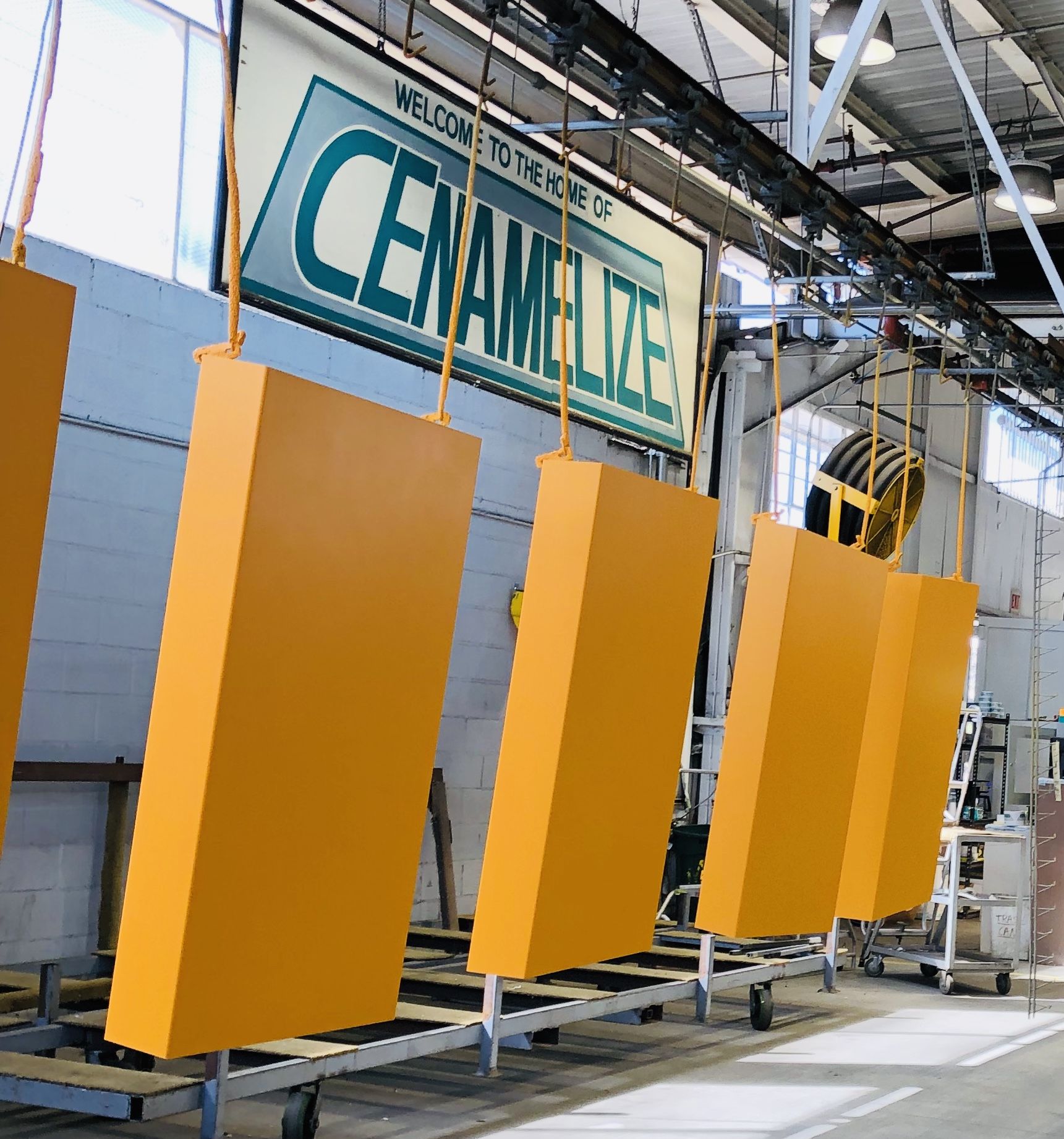 The interior of the Certified Enameling, Inc. facility with yellow-coated panels drying under a sign that says, "Welcome to the home of Cenamelize"
